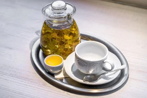 Hot linden-flower tea in transparent glass teapot, small cup of honey, and em Stock Photos