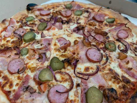 A hot rustic pizza topped with sliced sausage, smoked bacon, red onion, and Stock Photos