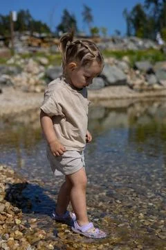 On a hot summer day, a child walks along the edge of the water on the rocky Stock Photos