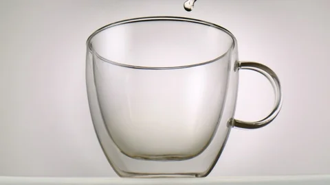 Hot tea being poured inside a glass in front of white background in slowmotio Stock Footage 99701226