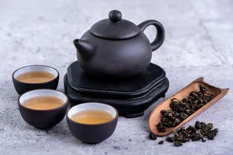 Hot tea in black teapot and cups and dry tea leaves over bright gray cement b Stock Photos