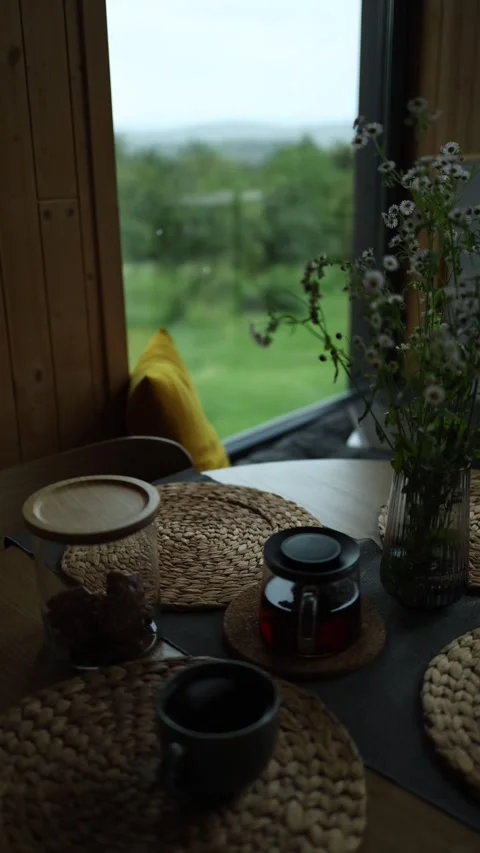 Hot tea in a mug and a kettle lies on the table near a vase with flowers raining Stock Footage 246443245
