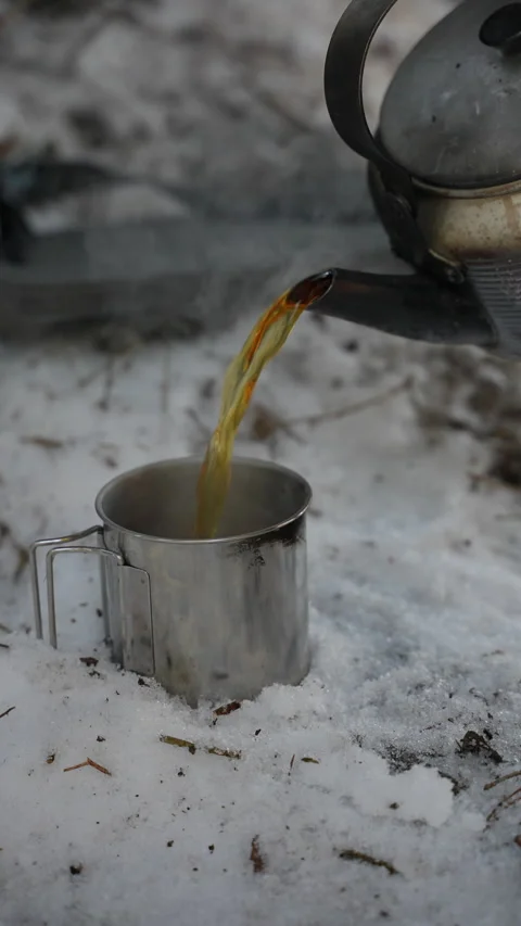 Hot tea is poured from a camping kettle into a metal mug 库存影片 329611657
