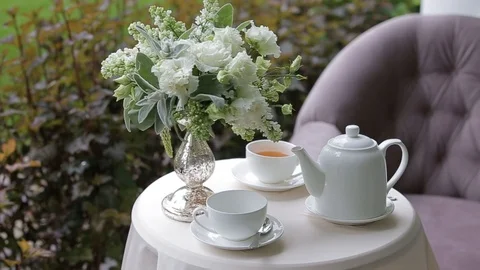 Hot tea in white cups served outdoors on a white table decorated with a bouquet Stock Footage 115936135