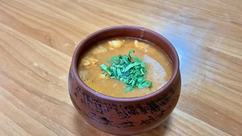 Hot thick soup garnished with fresh chopped herbs in a rustic clay pot Stock Footage 338045486