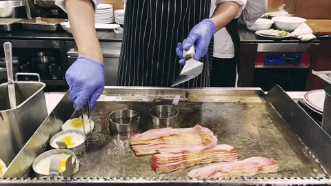 Hotel Chef cooking fried eggs and fried bacon in pan in kitchen. Stock Footage 252083697