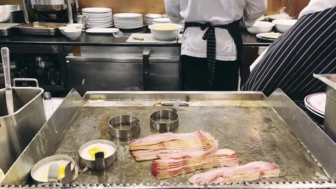 Hotel Chef cooking fried eggs and fried bacon in pan in kitchen. Stock Footage 260634748