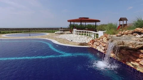 Hotel pool by the seaside with water cascading over artificial waterfall Stock Footage 71965994