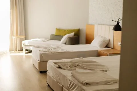 The hotel room features two unmade beds with fresh linens and a cozy seating  Stock Photos
