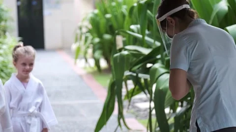 Hotel staff greets two cute sister kids wearing little bathrobes walking to spa Stock Footage 139048218