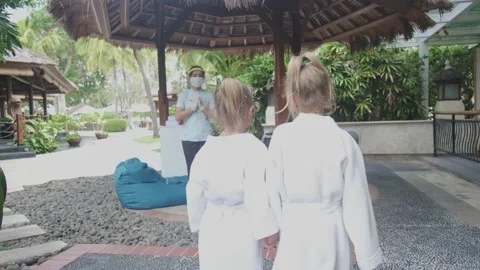 Hotel staff greets two cute sister kids wearing little bathrobes walking to spa Stock-Footage 139048281