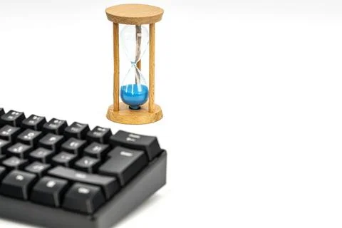 Hourglass with blue sand timer standing beside a black computer keyboard Stock Photos