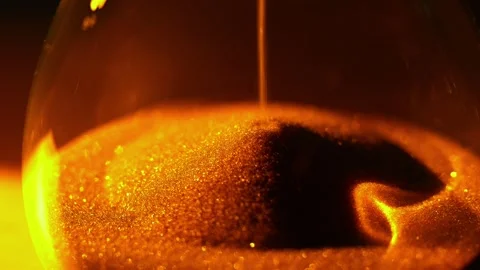 An hourglass is dramatically lit by a warm, golden light against a dark Stock Footage 319949261
