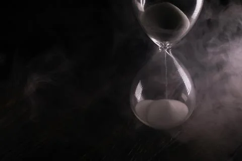Hourglass with Flowing Sand and Dramatic Smoke in Dark Ambience Stockfoto's
