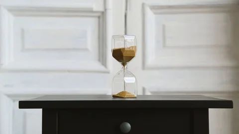 Hourglass light background, stand on a black bedside table. golden sand fray. Stock Footage 109258252