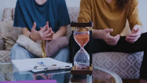Hourglass measuring time during couple's therapy session Stock Footage 339612738