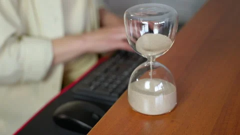 Hourglass measuring time while office worker typing on a keyboard Stock Footage 334578402