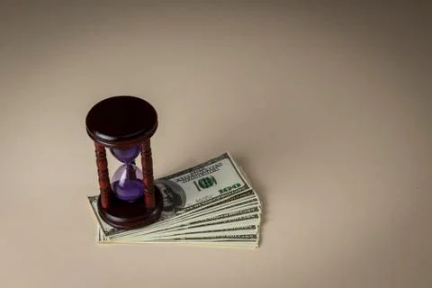 An hourglass on a pack of dollars is on the table Stock Photos