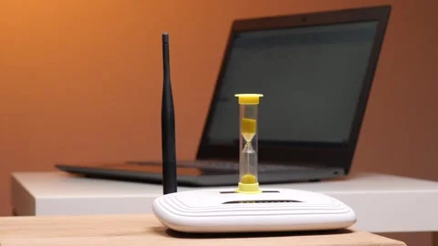 Hourglass with sand falling placed on a wireless internet router, symbolizing Stock Footage 347236278