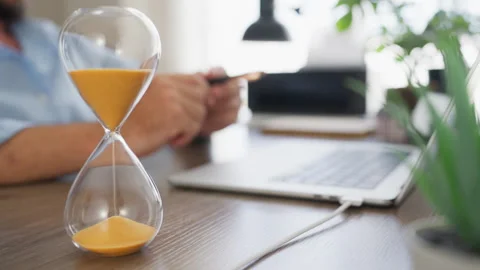 Hourglass in sharp focus with a businessman working on a laptop in the back.. Stock Footage 341624421