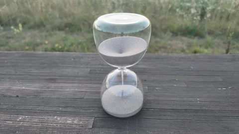 Hourglass timer with sand flowing on weathered wooden planks outdoors Stock Footage 340631283
