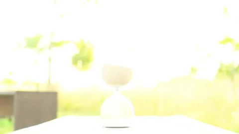 Hourglass timer on a wooden table with blurred natural background. Overexposed Stock Footage 340631387