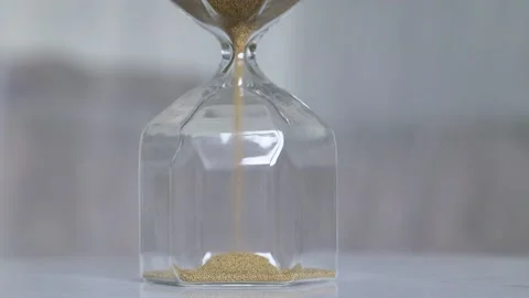 Hourglass on a white table in a bright room. An hourglass with golden sand stand Stock Footage 155377448