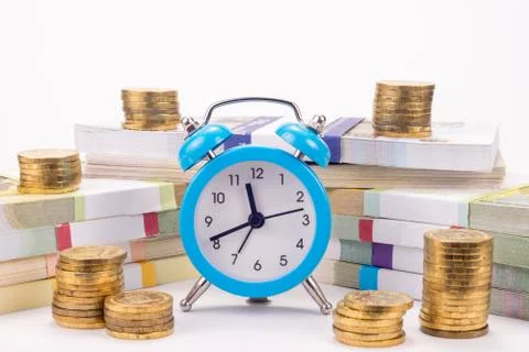 Hours stand before a pack of notes, around there are stacks of coins Stock-Fotos