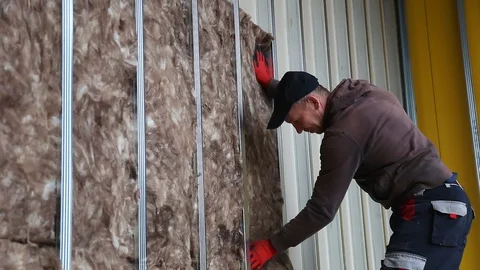 House attic insulation - construction worker installing rock wool in mansard Stockbeeldmateriaal 128497020