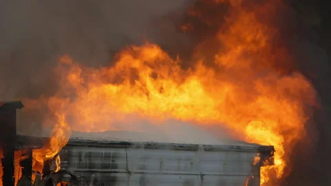 A house engulfed in flames during the day. Slow motion footage of a large Stock Footage 229816772