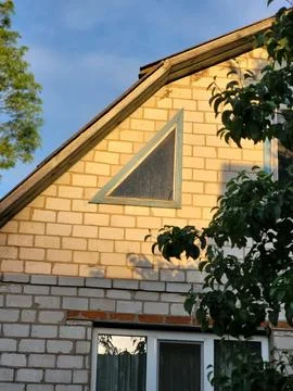 House facade with a triangular window on a yellow brick wall, rural architecture 库存照片