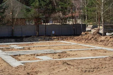 A house foundation under construction surrounded by forest and nearby house.. Stock Photos