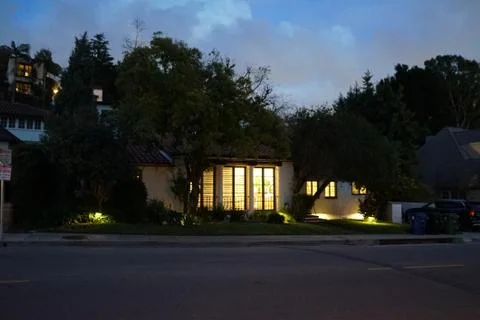 House with lights in big windows on the street at the bottom of the hill Stock Photos