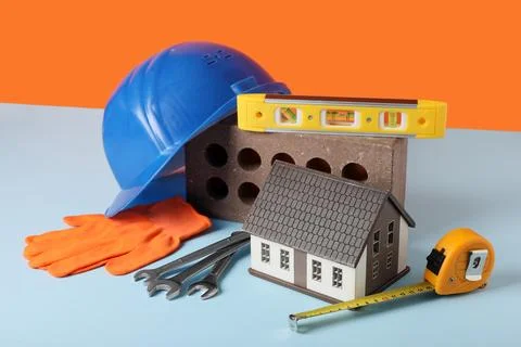 House model, hardhat and construction tools on blue table against orange back Stock Photos