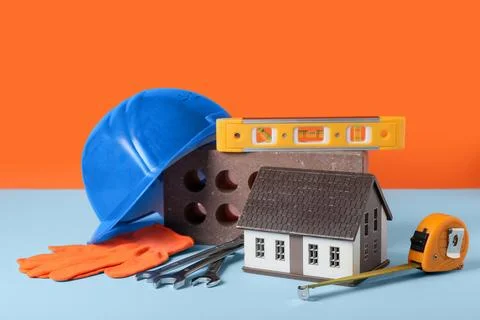 House model, hardhat and construction tools on blue table against orange back Stock Photos