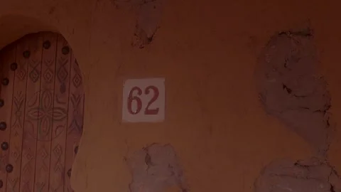 House number 62 on weathered mud wall beside carved wooden door in Morocco Stock Footage 336001387