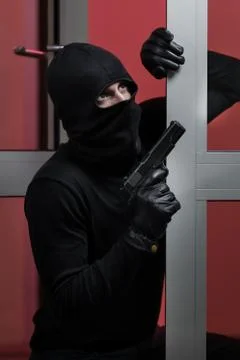 House robbery by man in a black jacket and black mask holding black gun. Stock Photos