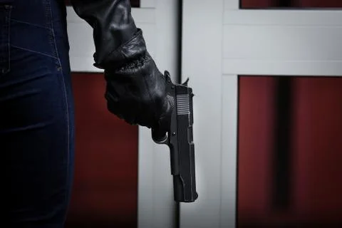 House robbery by man in a black jacket and black mask holding black gun. Stock Photos
