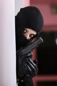 House robbery by man in a black jacket and black mask holding black gun. Stock Photos