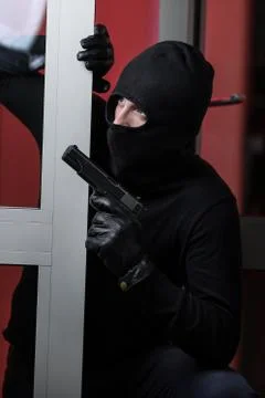 House robbery by man in a black jacket and black mask holding black gun. Foto stock
