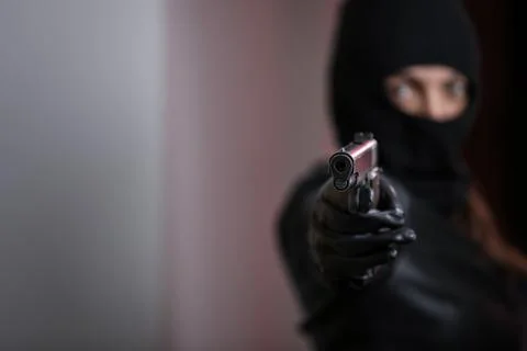 House robbery by woman in a black jacket and black mask holding black gun. Stock Photos