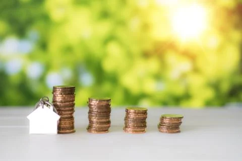 House shape keychain lean on Stacks of gold coins with green bokeh background 库存照片