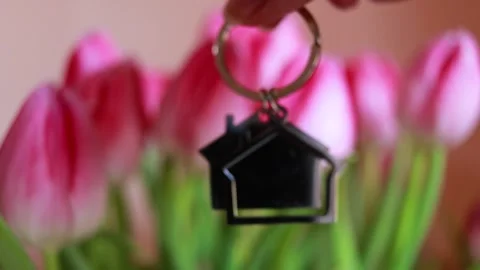 House shaped keychain held in hand with pink flowers in background, real estate Stock Footage 330663101