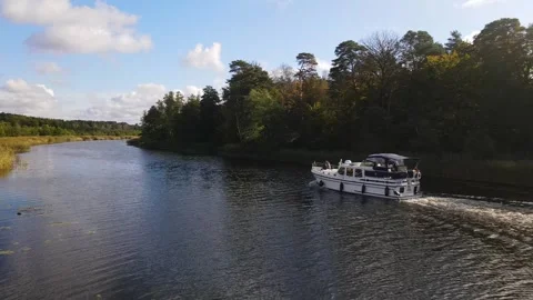Houseboat Sails a river in between Reed and Autumn Forest, Germany, 4K Drone Stock Footage 279763394