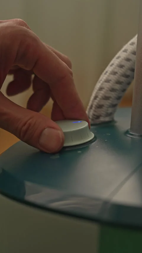 Housekeeper hand adjusting power button on clothes steamer, setting stage for Stock Footage 304875869