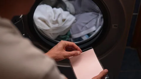 Housekeeper placing white laundry detergent sheet, preparing to load washing Stock Footage 292449364