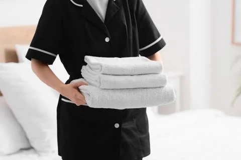 Housekeeper in uniform holding a stack of clean white towels in a hotel room, Stock Photos