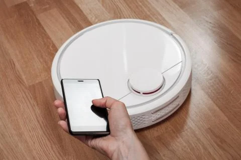 Housekeeper using mobile to control black robotic vacuum cleaner. modern smar Stock Photos