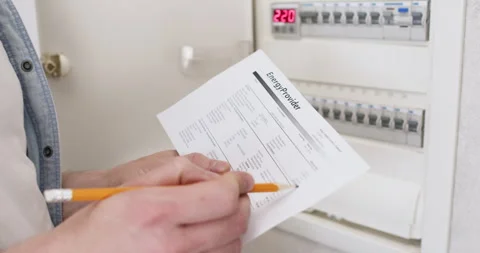 Houseowner processes electricity bill standing in front of switch box Stockbeeldmateriaal 302027853