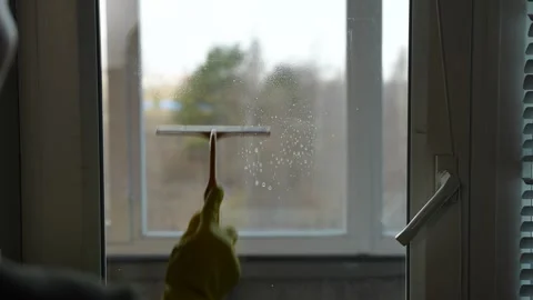A housewife sprays cleaning solution onto a window using a spray bottle and Stockbeeldmateriaal 308020197
